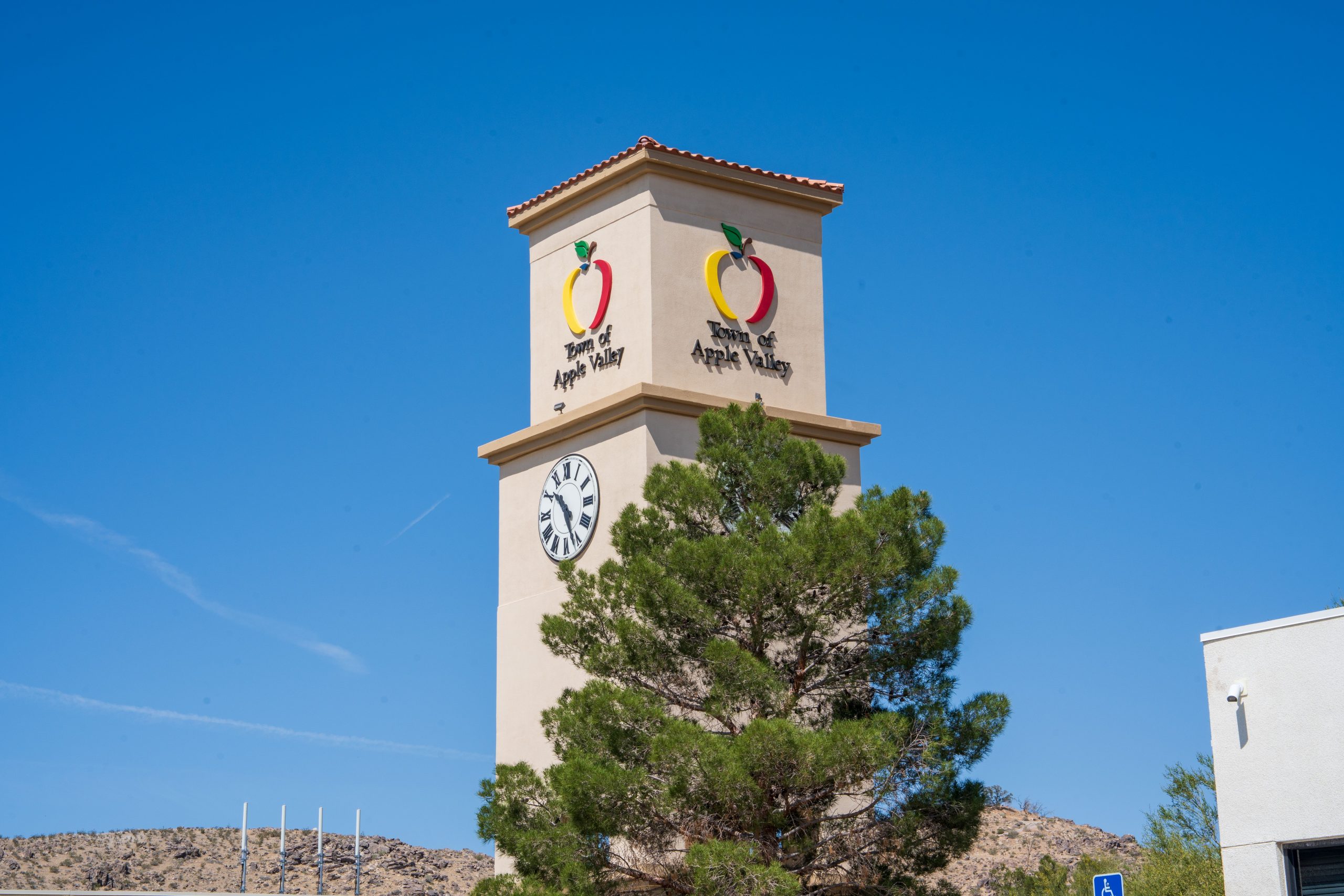 A clock tower displaying the Town of Apple Valley logo. A tree is partially covering the tower.