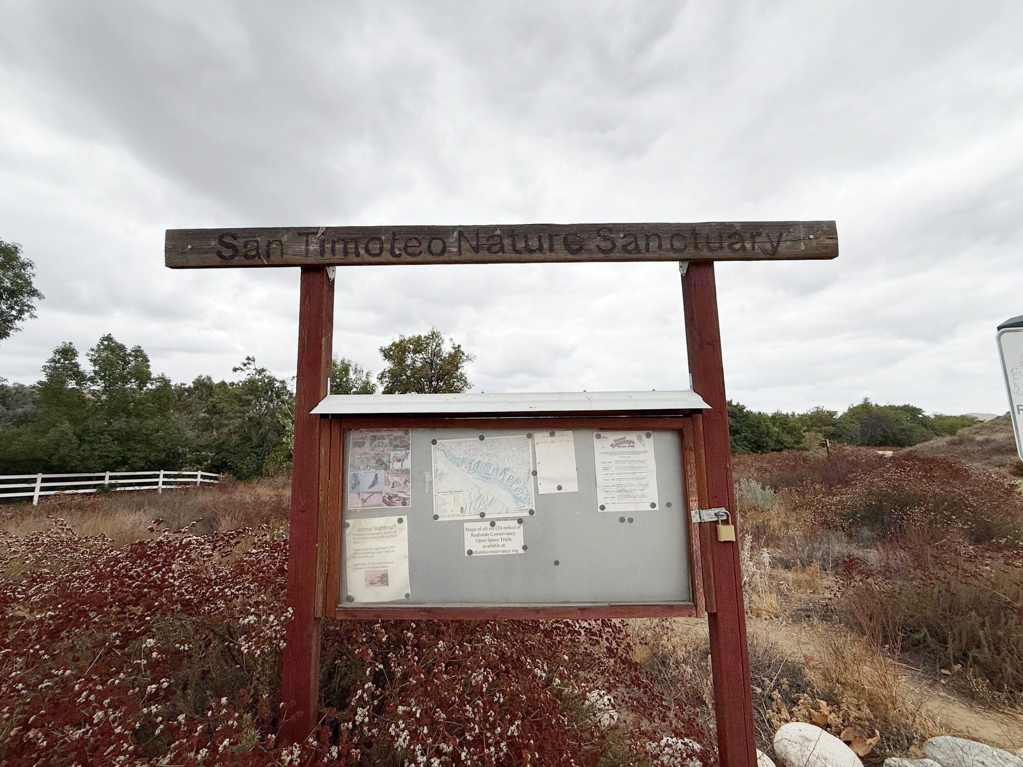 A wooden sign reading "San Timoteo Nature Sanctuary" mounted above a bulletin board displaying maps and information.