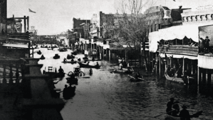 Black and white photo of a flooded street with individuals in rowboats.