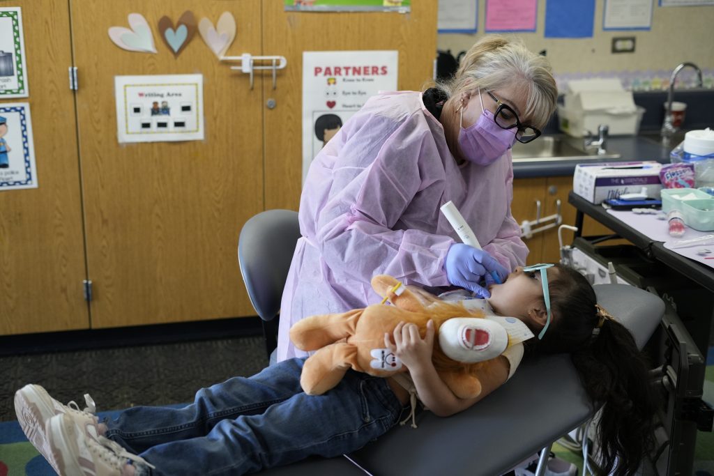 Dental provider in protective gear checking a young child’s teeth.