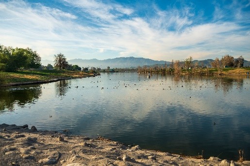 A landscape of a lake with mountains in the background and a hill grass area on the left under a blue cloudy sky.