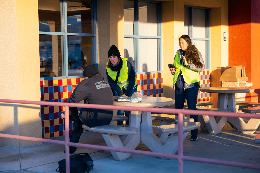 Two female volunteers are seen talking to a homeless man outside a fast food restaurant dining area.