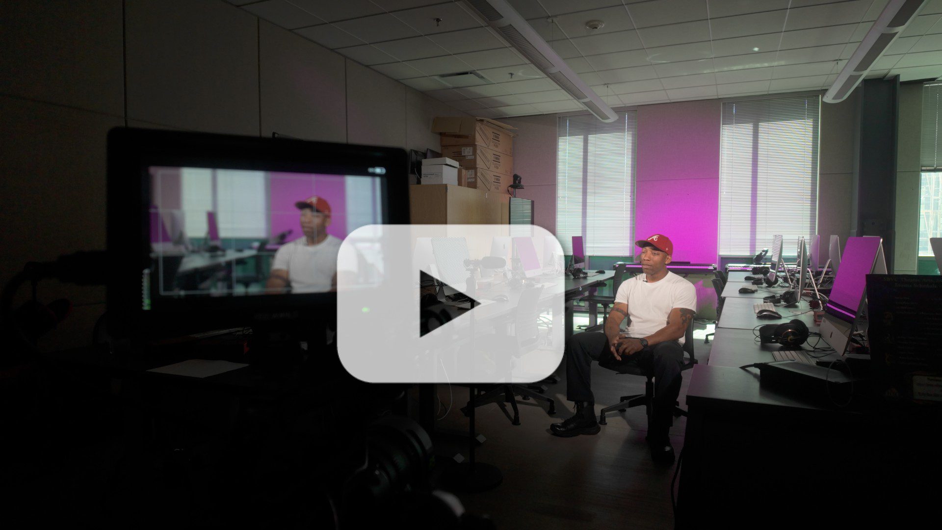 Video thumbnail showing a man being interviewed in a computer lab, with filming equipment visible in the foreground.