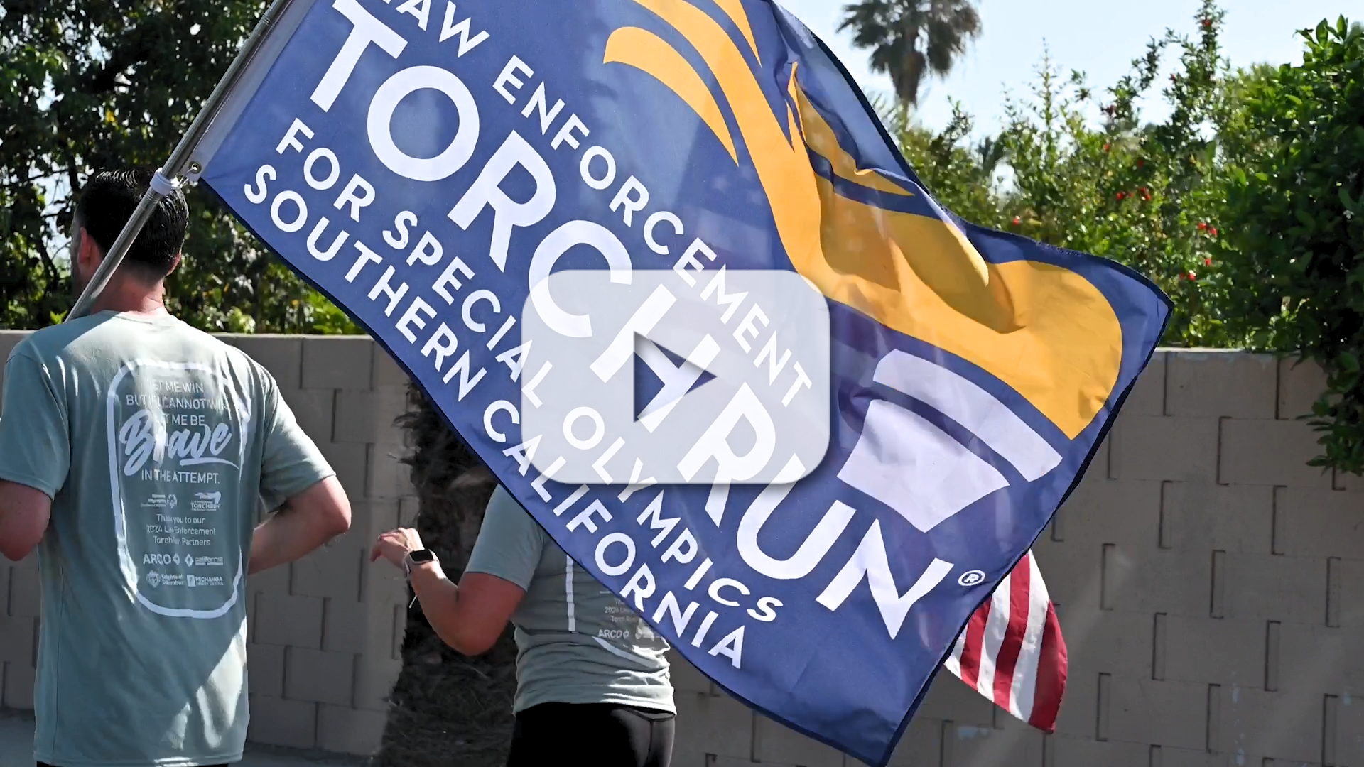A photo of a man running holding a flag that says law enforcement torch run with a woman next to him running outside.