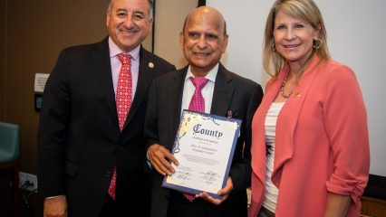 A photo of Fifth District Supervisor Joe Baca, Jr., Dr. Dev A. GnanaDev and Third District Supervisor and chairman Dawn Rowe.