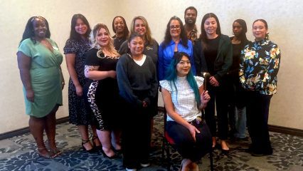 Eleven women and one man stand in a group posing for the camera.