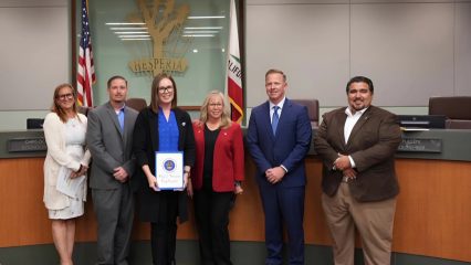 Group of six people standing and smiling in a council room, while a woman holds a proclamation letter for Child Abuse Prevention Month.