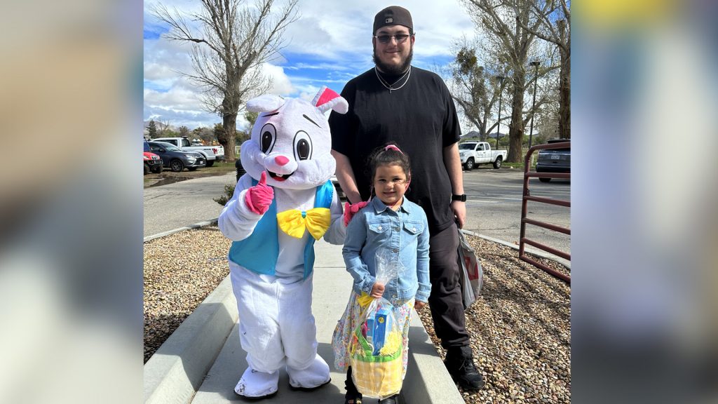A young girl holds an Easter basket standing next to the Easter bunny and a man at Mojave Narrows Regional Park.