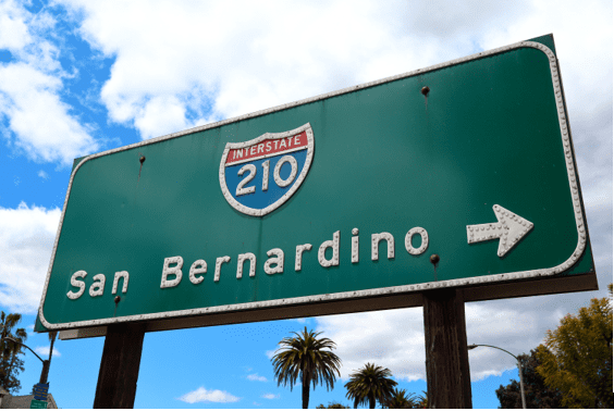 Interstate 210 road sign with an arrow pointing right and text that says San Bernardino. Also visible are palm trees in the background.