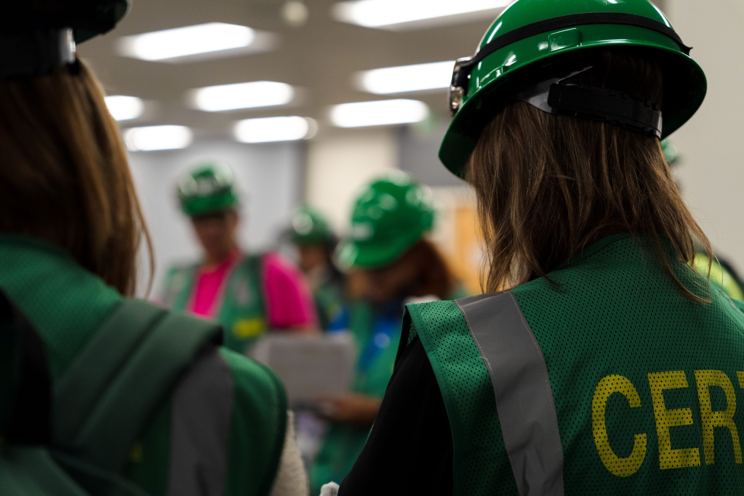 Participants wearing green helmets and vests with "CERT" written on them. The focus is on individuals in the foreground, with others blurred in the background.