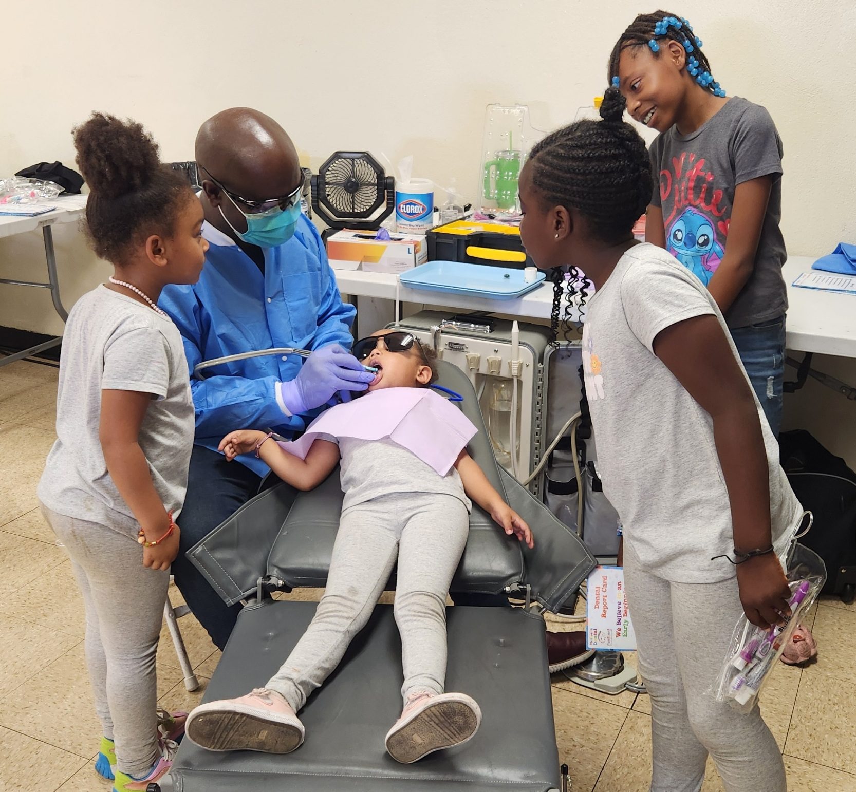Dentist examining a child’s teeth as other children watch.