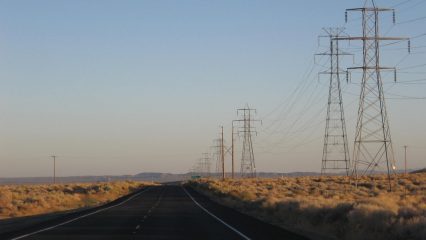 A highway surrounded by tall electrical pylons and sparse vegetation.