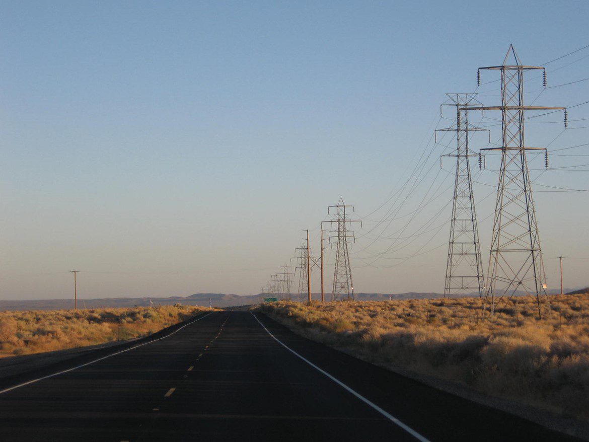 A highway surrounded by tall electrical pylons and sparse vegetation.