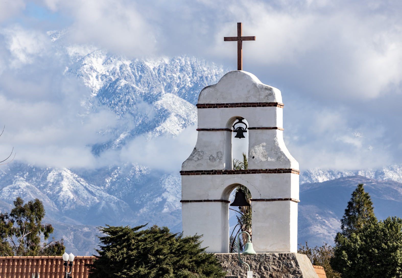 A bell tower with a cross on top and snowy mountains in the background.