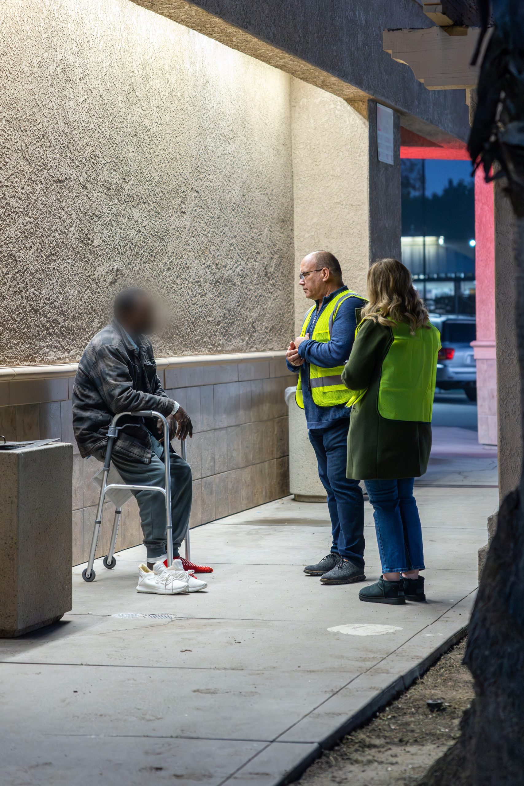 Two individuals in reflective vests standing outside at a gas station interacting with a homeless person.