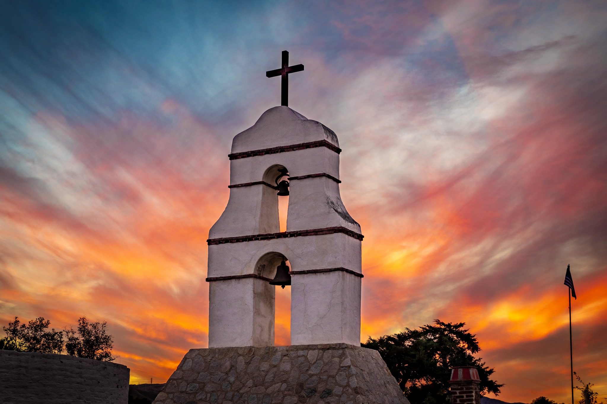 An image of a bell tower with a cross on top taken at sunset.