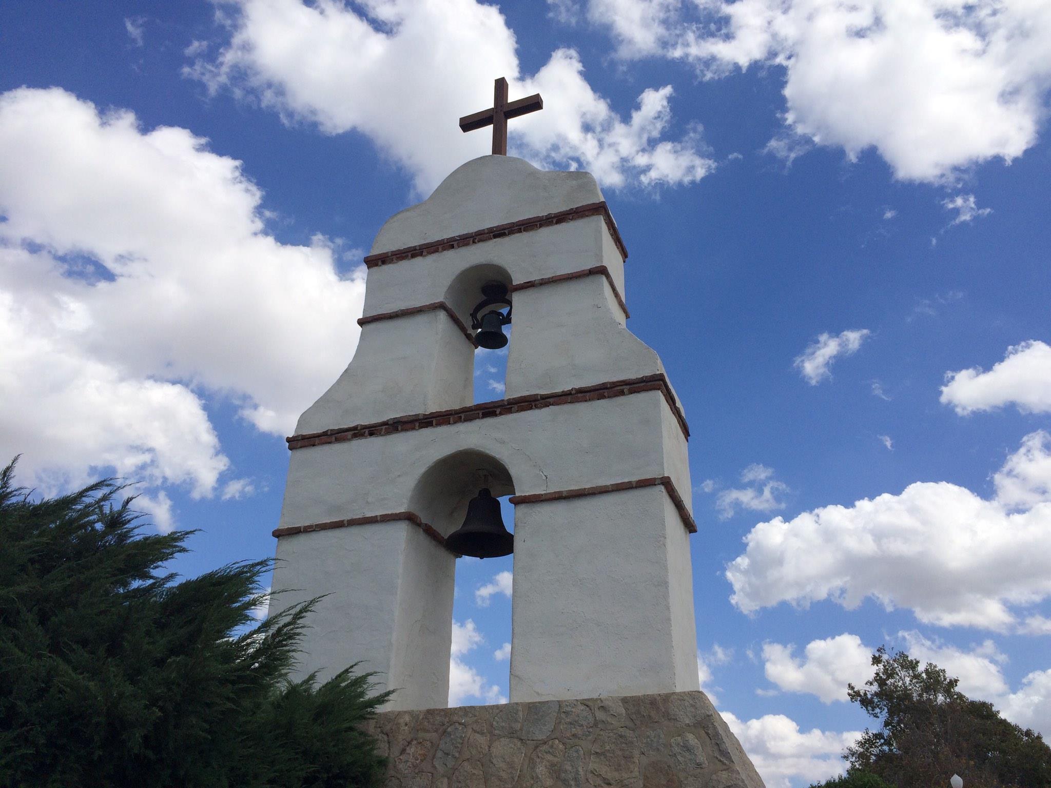 A bell tower with a cross on top and a blue sky filled with clouds in the background.