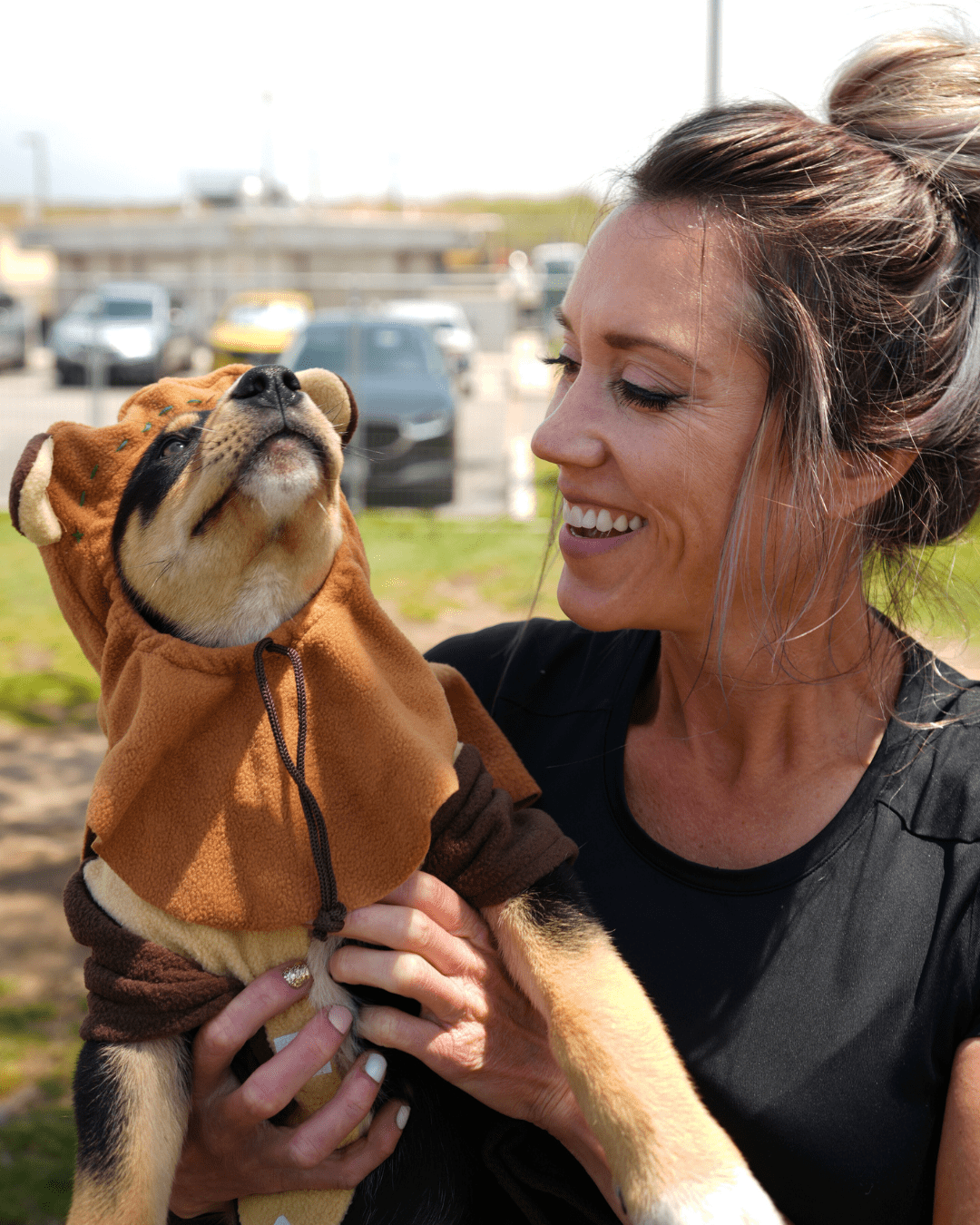 Black and brown fur puppy wearing an ewok custom. Held by a person wearing a black shirt.