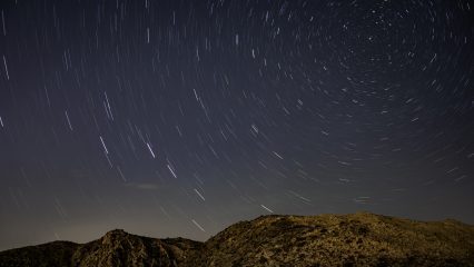 A mountain silhouette beneath a swirling star trail in a night sky, showcasing celestial movement above the landscape.