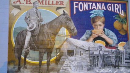 A mural depicting historical scenes, including a person named A.B. Miller on a horse, and a child drinking juice from an orange with text that says “Fontana Girl” above her. The artwork also features an old mill and workers in a field.