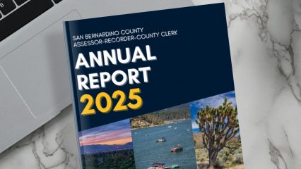 A laptop, notebooks, cup of coffee, and San Bernardino County Assessor-Recorder-County Clerk Josie Gonzales’s 2025 annual report on a marble table.