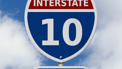 A road sign for Interstate 10 featuring a blue shield with a red top displaying the number "10" and the word "Interstate."