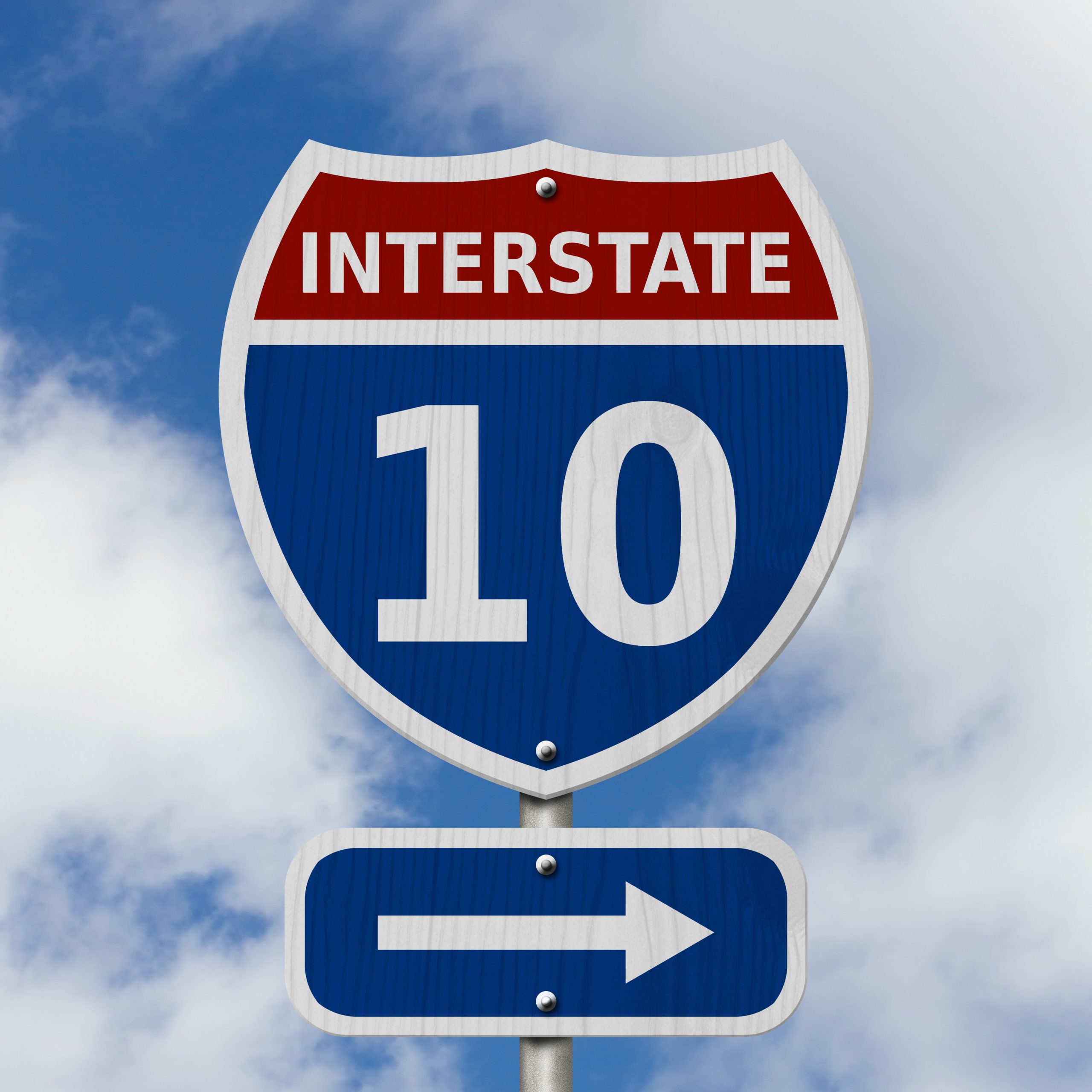 A road sign for Interstate 10 featuring a blue shield with a red top displaying the number "10" and the word "Interstate."