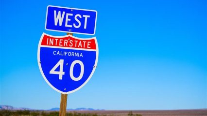 Road sign that says 'West Interstate 40” with a desert landscape in the background.