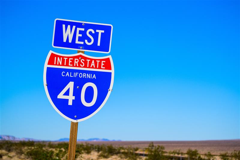 Road sign that says 'West Interstate 40” with a desert landscape in the background.