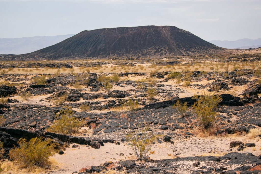 A picture of Amboy Crater in the Mojave Desert featuring a volcanic cone surrounded by lava fields.
