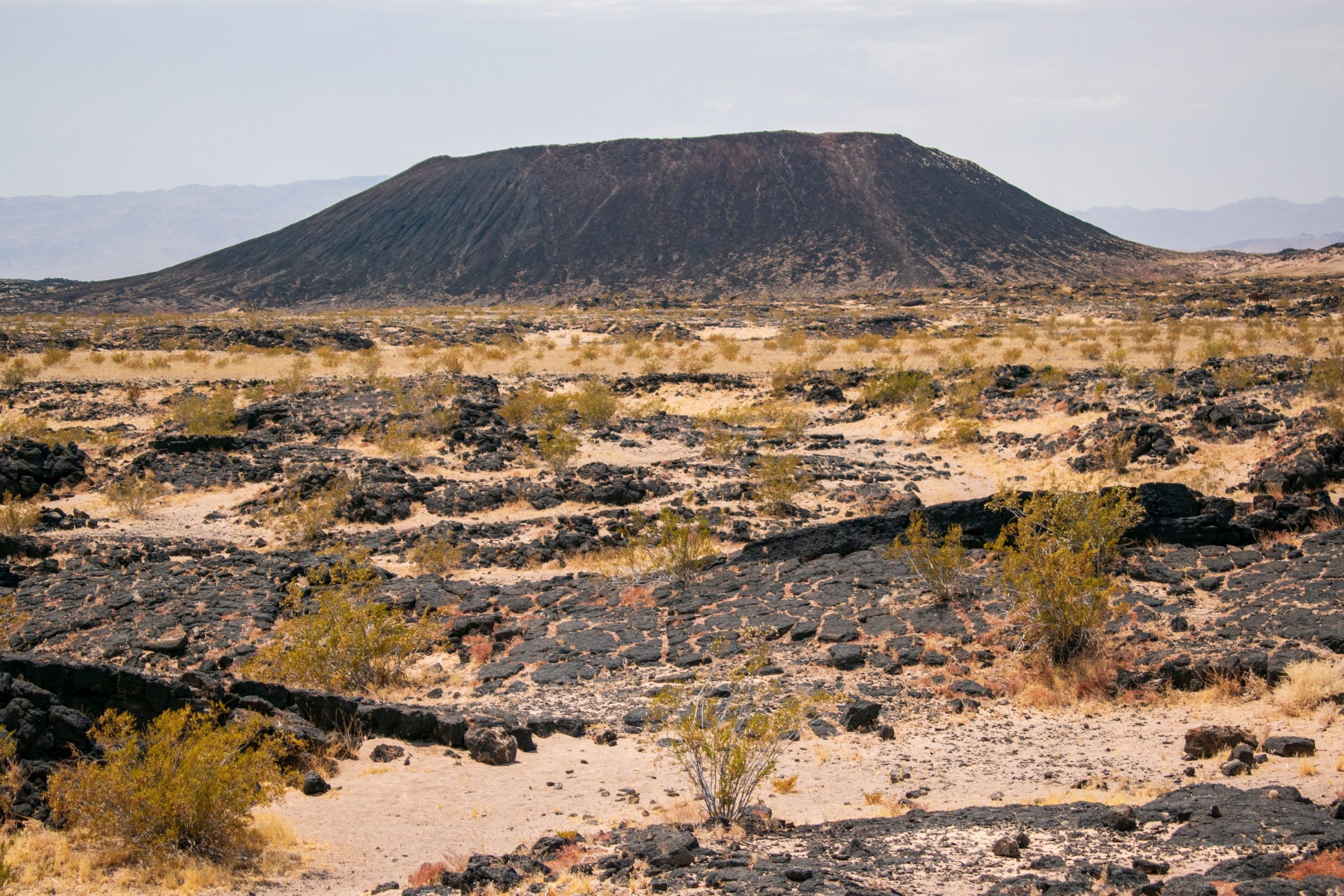 A picture of Amboy Crater in the Mojave Desert featuring a volcanic cone surrounded by lava fields.