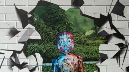 A robot stands in a garden, visible through a large hole in a gray brick wall, surrounded by jagged, shattered fragments, evoking surprise.