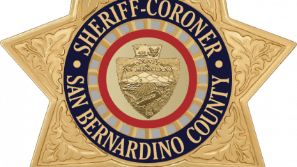 Golden star-shaped badge with leaf patterns, labeled "Sheriff-Coroner San Bernardino County" around the county seal depicting a mountain and field.