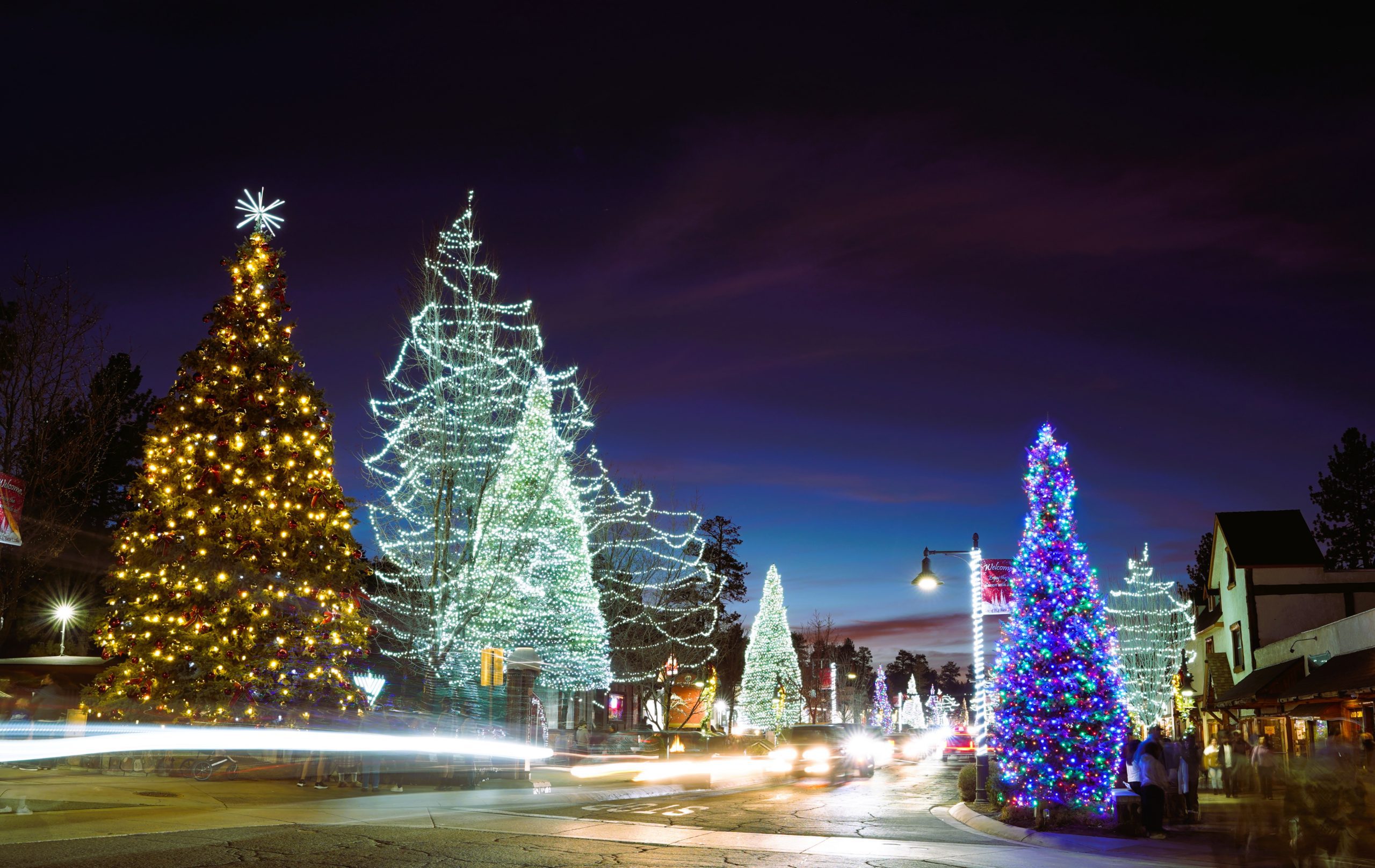 A view of a street in Big Bear Lake with multiple Christmas trees covered in colorful lights.