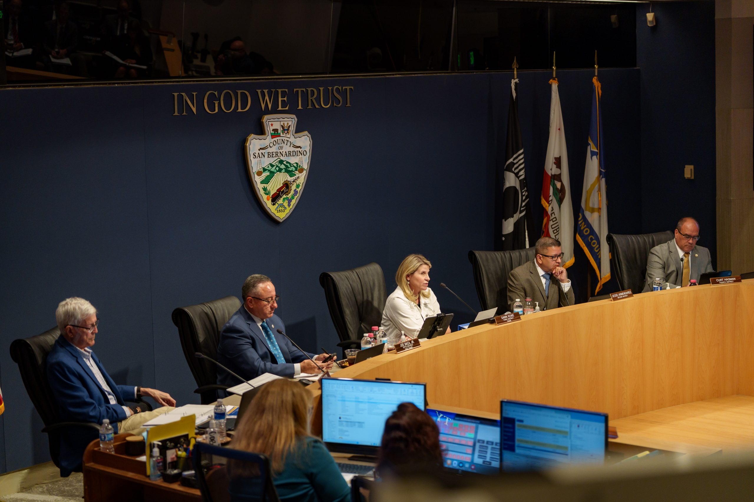 Officials seated at a dais beneath “In God We Trust” and the San Bernardino County seal.
