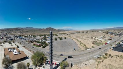A panoramic view of the World's Tallest Thermometer in Baker. The image also includes various buildings and a roadway with vehicles.