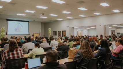 Attendees sit at long tables in a conference room during the May 2024 Behavioral Health Commission meeting.