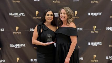 Two women in elegant black dresses pose with an award against a backdrop featuring "Inland Empire Magazine" and "Pechanga Resort Casino" logos.