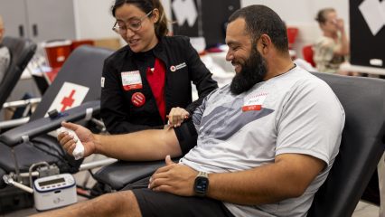 A person with a bandaged arm relaxes on a chair, smiling, while another person wearing a Red Cross badge engages in conversation.