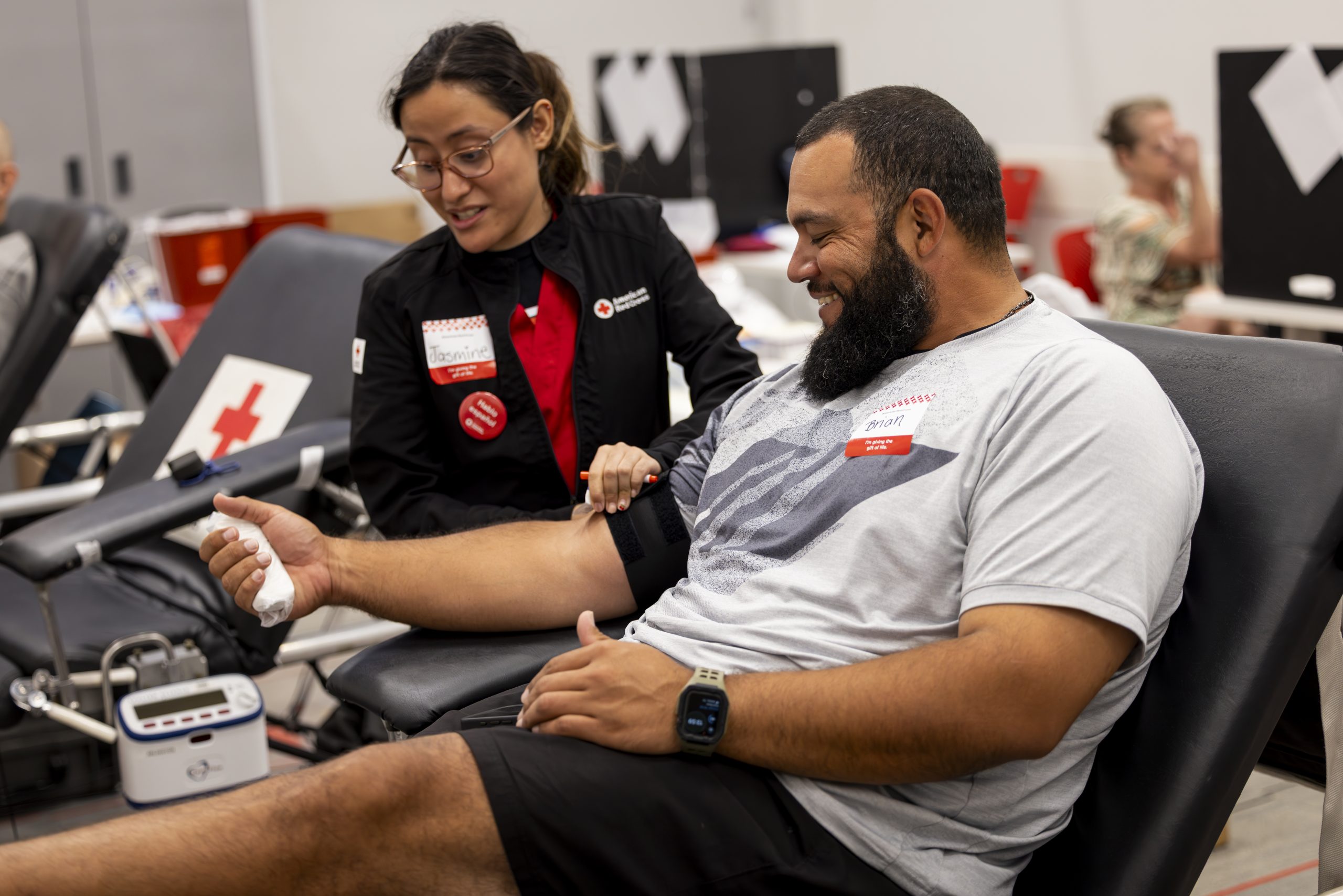 A person with a bandaged arm relaxes on a chair, smiling, while another person wearing a Red Cross badge engages in conversation.