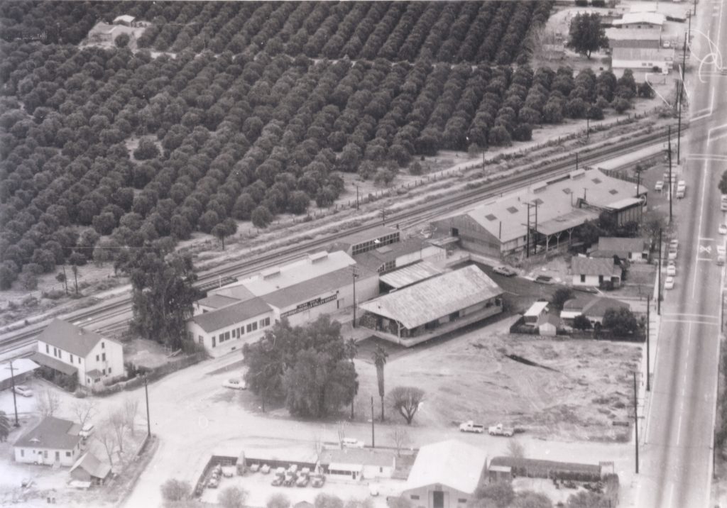 The image shows a number of industrial buildings surrounded by trees and train tracks.

