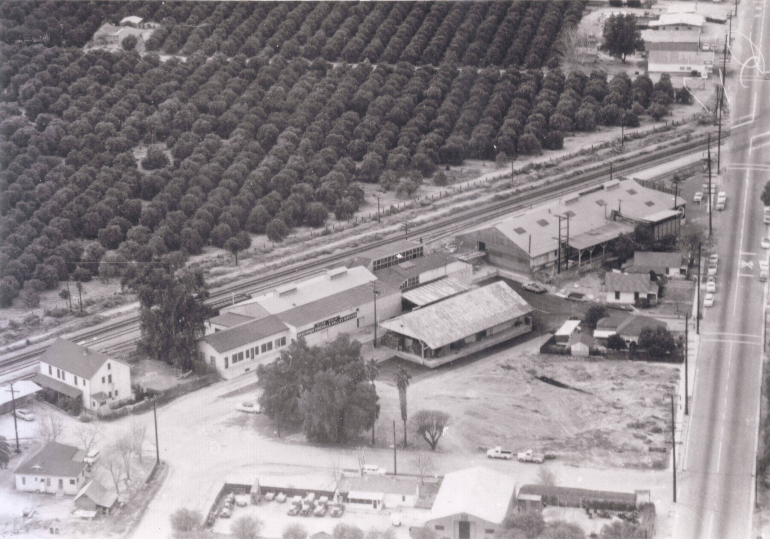The image shows a number of industrial buildings surrounded by trees and train tracks.