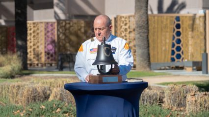 A man stands behind a table with a bell on it.