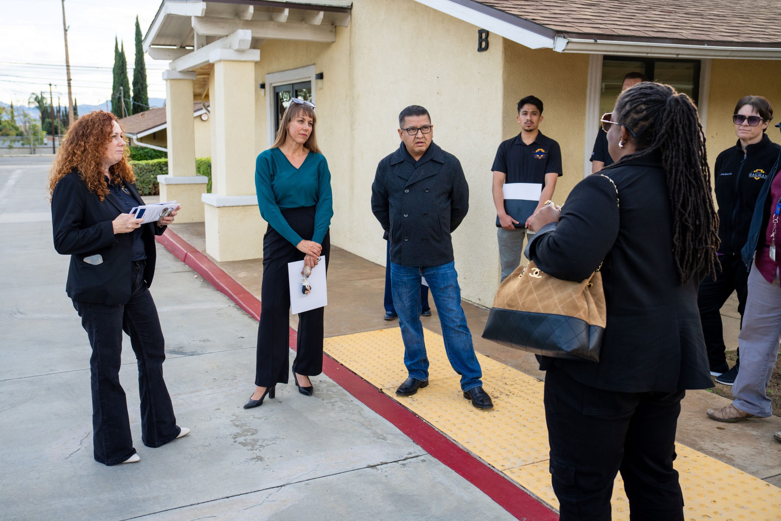 Group of professionals in a discussion outside a building, with some holding papers and attentive to the speaker.