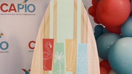 “CAPIO Advancing Public Sector Communicators” backdrop with colorful balloons and surfboard reading “Making Waves CAPIO 2026.”