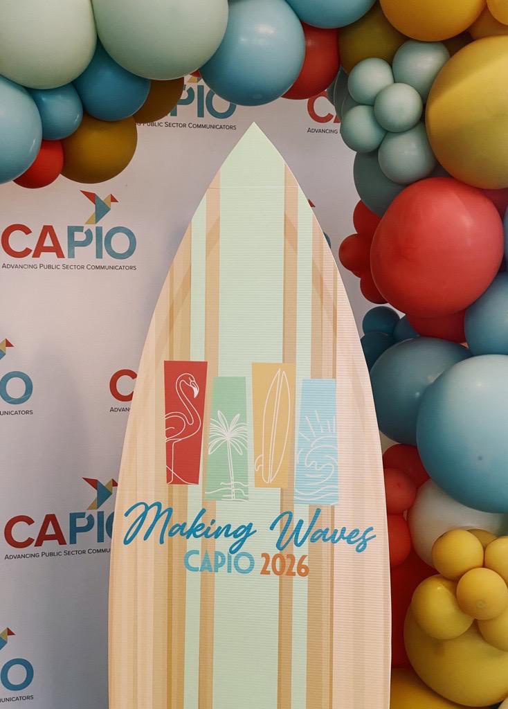 “CAPIO Advancing Public Sector Communicators” backdrop with colorful balloons and surfboard reading “Making Waves CAPIO 2026.”