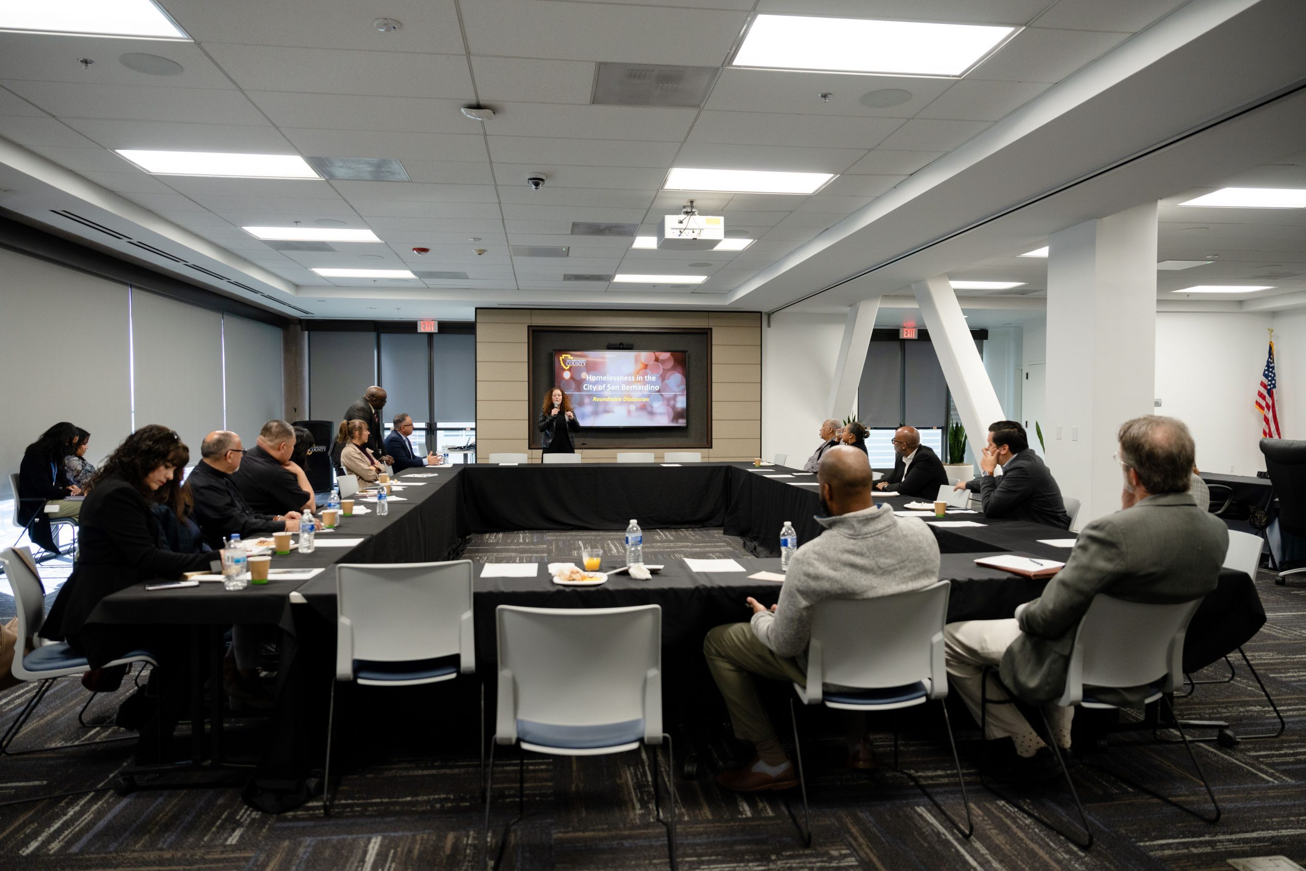 CDH Director Carrie Harmon stands at the front of a conference room, providing an update to the attendees at the homelessness roundtable.