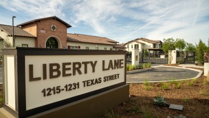 Entrance of Liberty Lane featuring a prominent sign in the foreground and a gated residential community in the background.