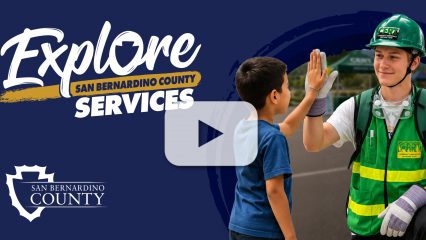 Man in hard hat and safety vests high-fives a child. “Explore San Bernardino County Services” logo and San Bernardino County logo.