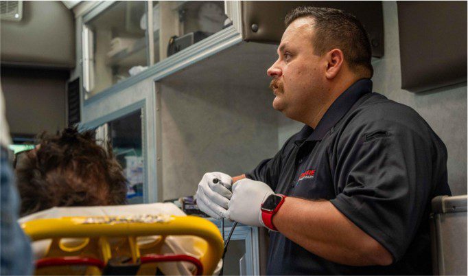 An emergency medical technician works beside a patient in an ambulance.